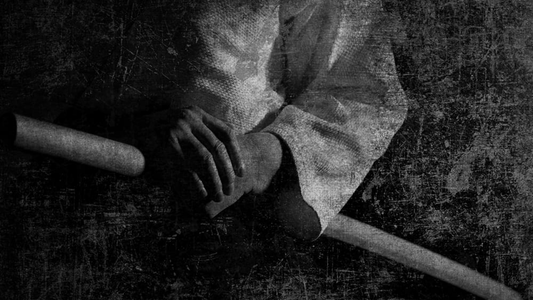 Black and white photograph of hands gripping a bokken wooden training sword, worn fabric sleeves visible, vintage grain texture
